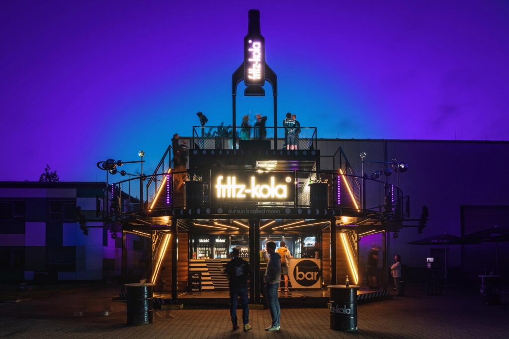 Beleuchteter Fritz-Kola Eventcontainer bei Nacht als Beispiel für kreativen Sonderbau und hochwertige Markeninszenierung.