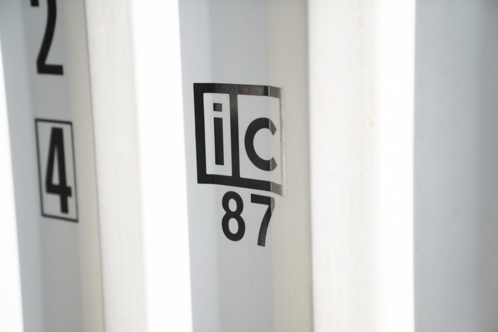Nahaufnahme der technischen Kennzeichnungen an der Tür eines grauen Spezialcontainers mit Fokus auf das UIC Bahnlogo sowie Gewichtsangaben für den intermodalen Verkehr