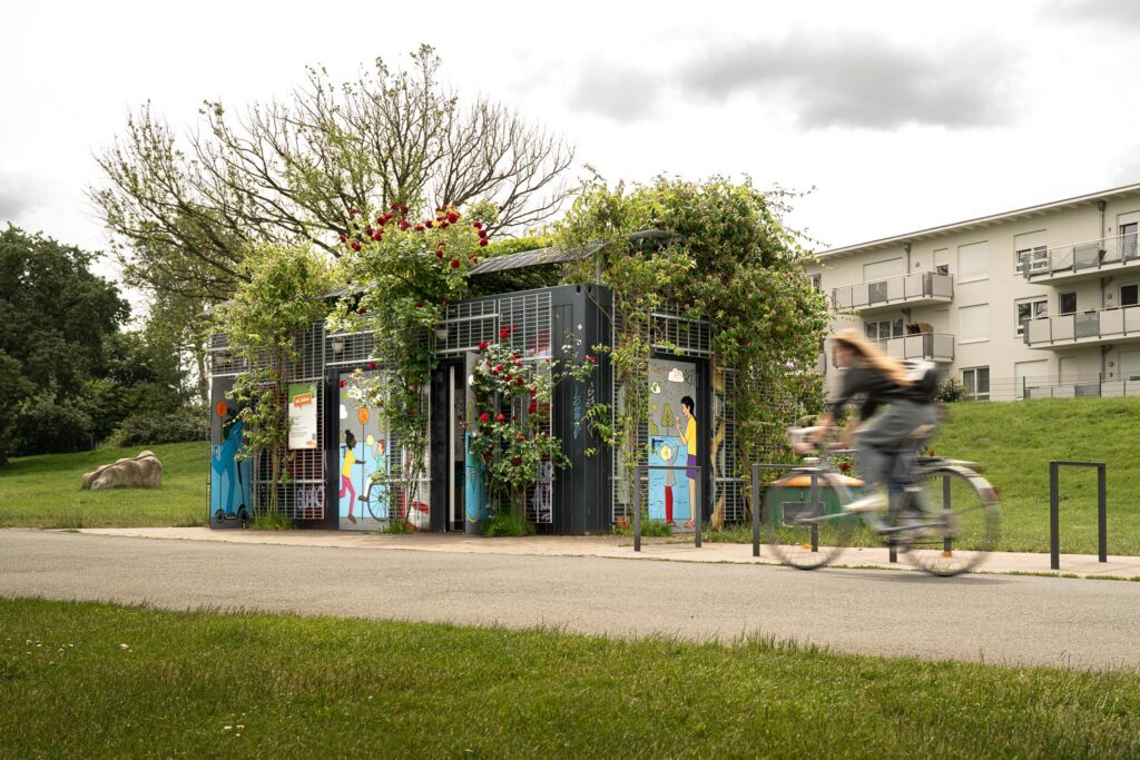 Öffentlicher WC-Container für die Bremer Stadtreinigung an der Weser seitlich frontal mit Radfahrer