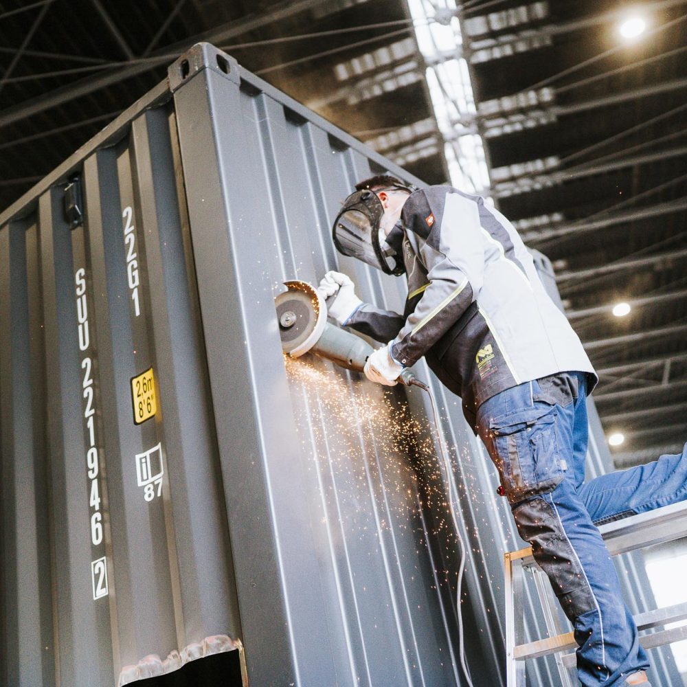 Mitarbeiter flext an Stahlcontainer und baut ihn um